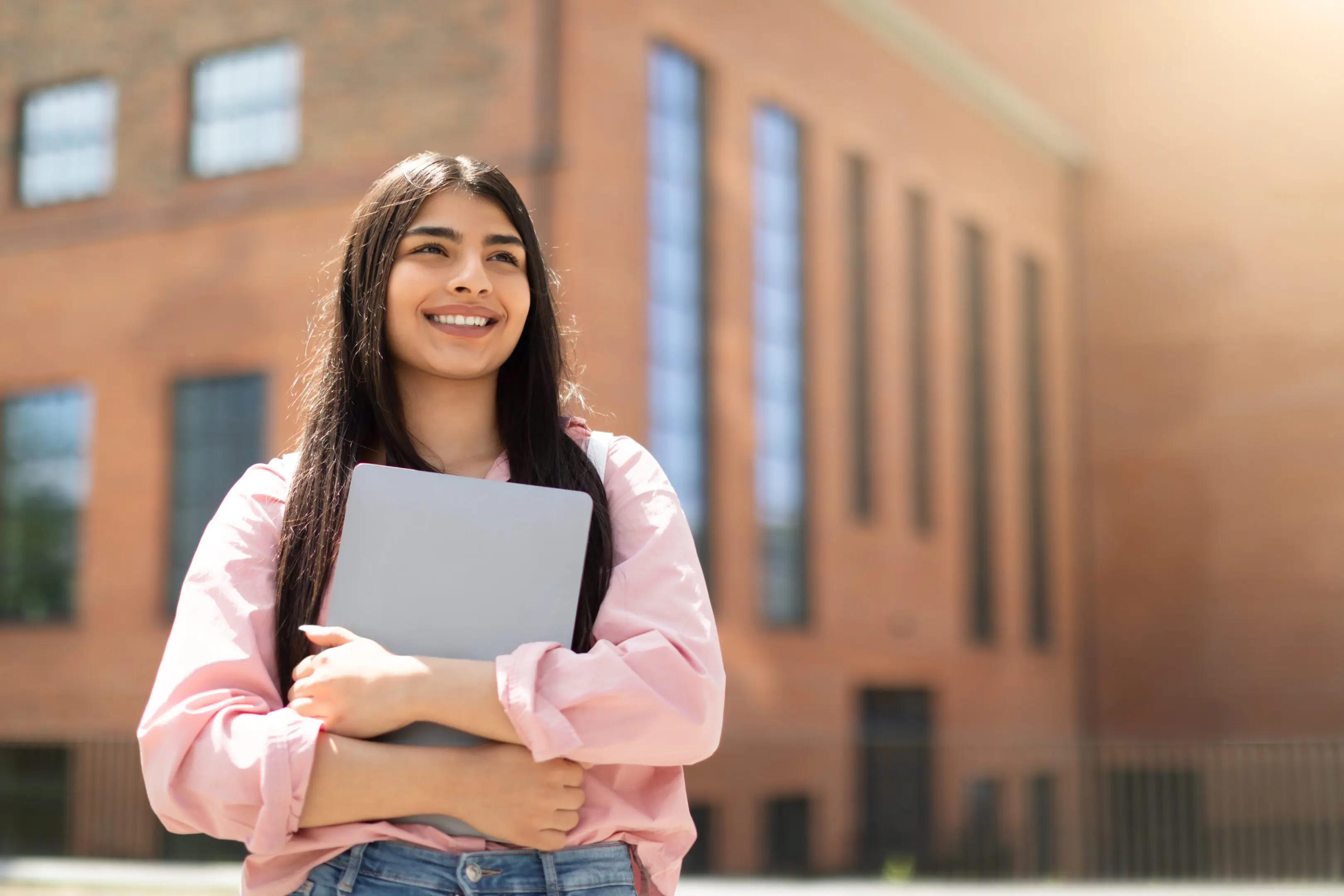 Young girl holding laptop and looking up A girl holding her laptop in front of a building.