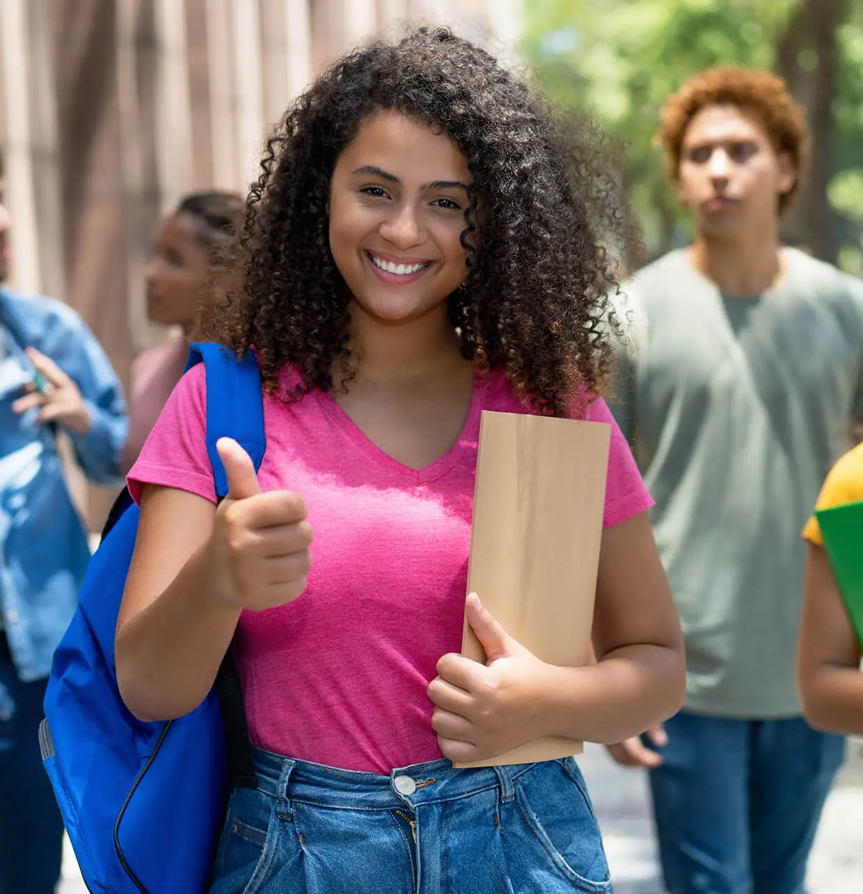 Student smiling with backpack and folder outside.