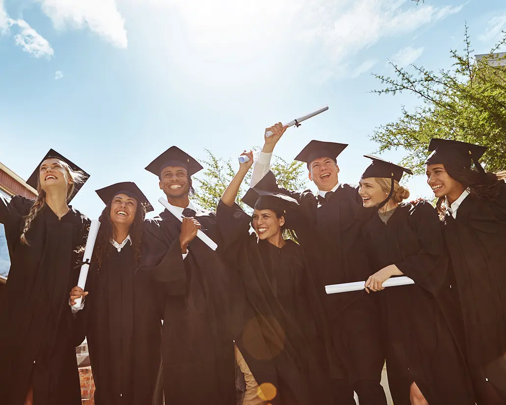 Graduates celebrating with diplomas outdoors, smiling.